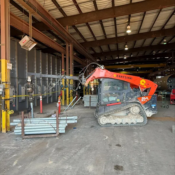 Installing helical foundation support inside a large industrial warehouse.