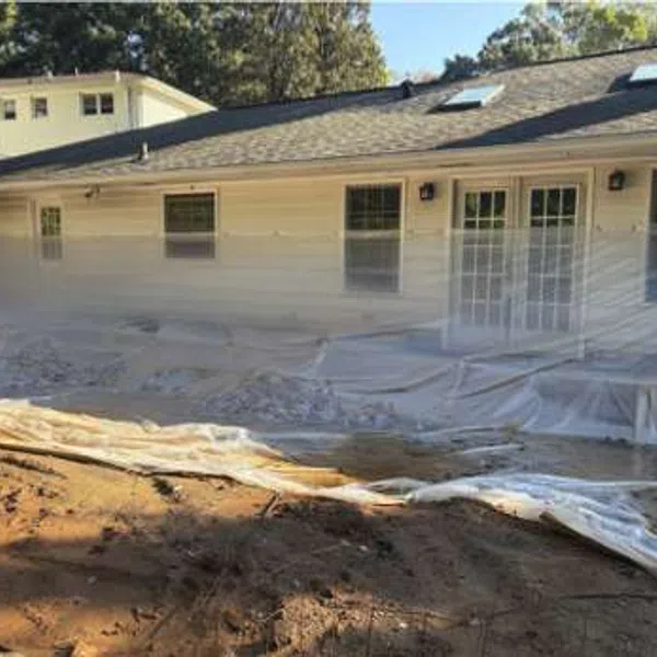 White house exterior with plastic sheeting covering windows and ground, likely for construction or painting protection.