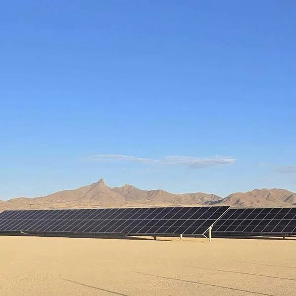 Solar panels installed on a desert landscape with mountains in the background under a clear blue sky.