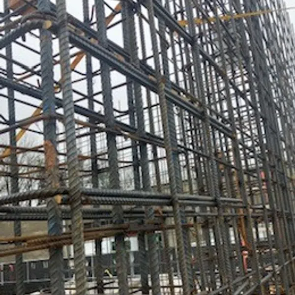 Close-up of steel rebar framework for concrete construction at a building site with overcast sky background.
