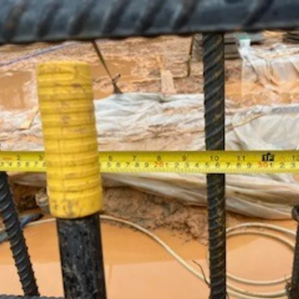 Measuring distance between rebar rods on a construction site using a yellow tape measure.