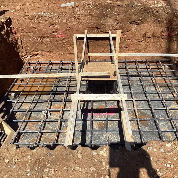Construction site with steel rebar grid and wooden planks setup for concrete foundation pouring.