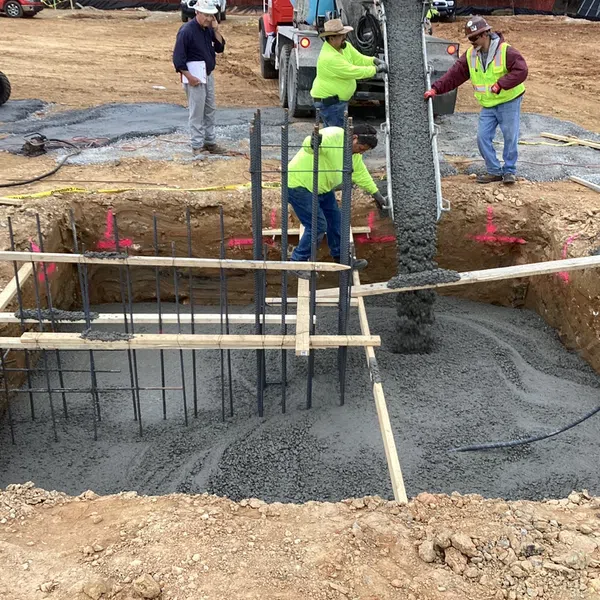 Construction workers pouring concrete into foundation with rebar and wooden supports at outdoor site.