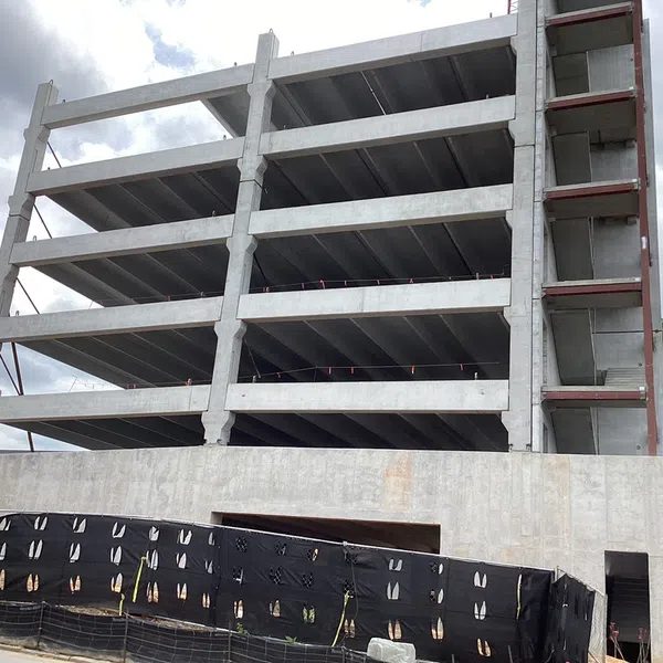 Multi-story concrete parking garage under construction with exposed floors and black safety netting on ground level.