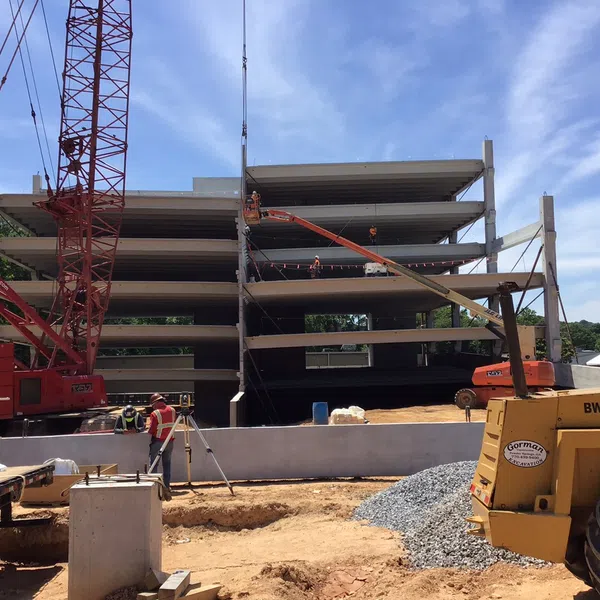 Construction site with workers, cranes, and machinery building a multi-story concrete structure under clear sky.
