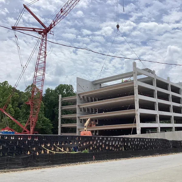 Construction site with multi-story concrete building framework and red crane against cloudy sky.