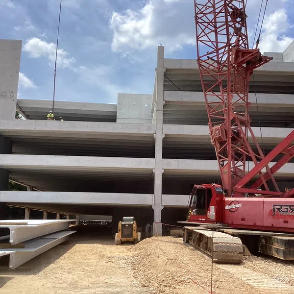 Concrete multi-level parking garage under construction with red crane and workers on site under blue sky