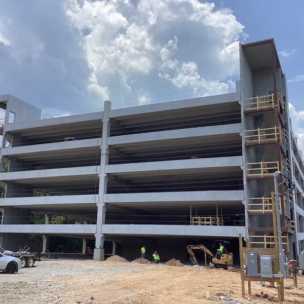 Multi-level concrete parking garage under construction with workers and machinery on site during daytime.