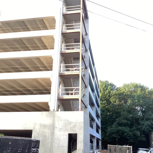 Multi-story concrete building under construction with exposed stairwell and construction materials on site.
