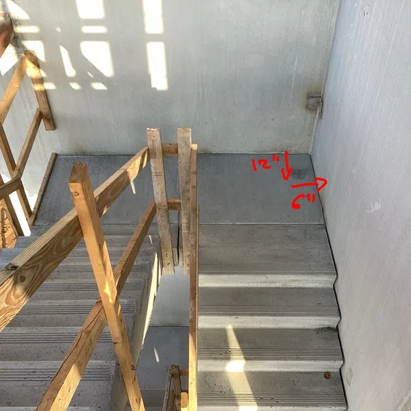 Concrete stairs with wooden handrails and red handwritten measurements of 12 inches and 6 inches on the wall.