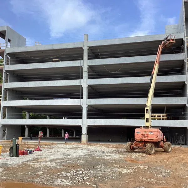 Concrete multi-story parking structure under construction with lift equipment and workers onsite.