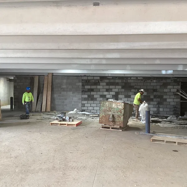 Construction workers in safety helmets working inside a building with concrete beams and cinder block walls under construction.
