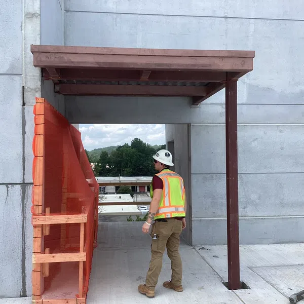 Construction worker in safety gear inspects partially built concrete structure with orange safety netting.