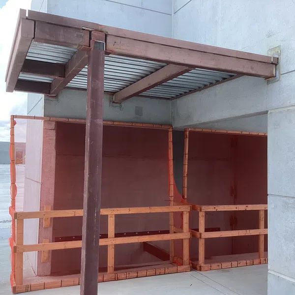 Construction site with wooden safety railings and a metal canopy attached to a concrete building wall.