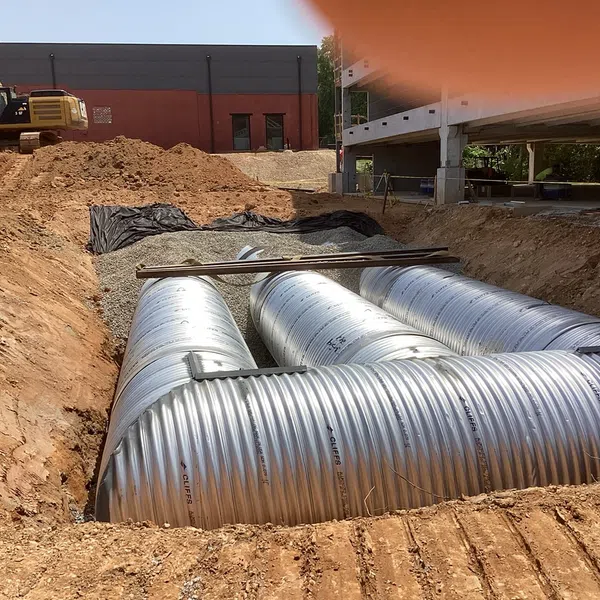 Large corrugated metal pipes being installed in an excavation site with construction equipment nearby