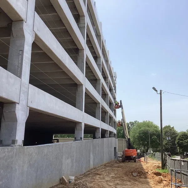 Multi-level concrete parking garage under construction with heavy machinery and workers on a sunny day.