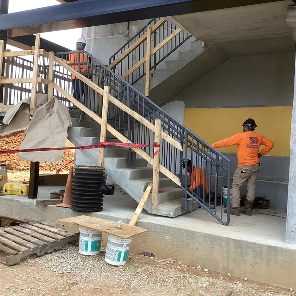 Construction workers installing a metal staircase railing at an unfinished building site with safety barriers.