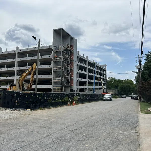Multi-story concrete parking garage under construction with construction equipment and a partly cloudy sky.