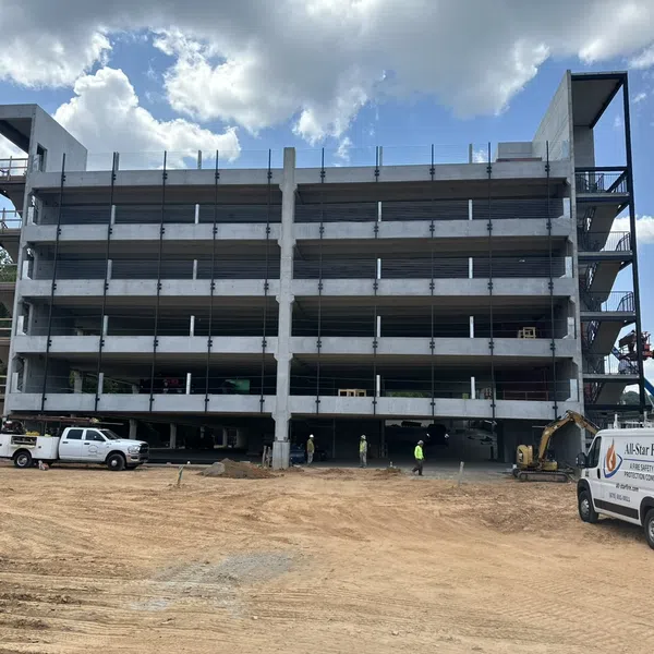 Multi-story concrete parking garage under construction with construction vehicles and workers on site under a partly cloudy sky