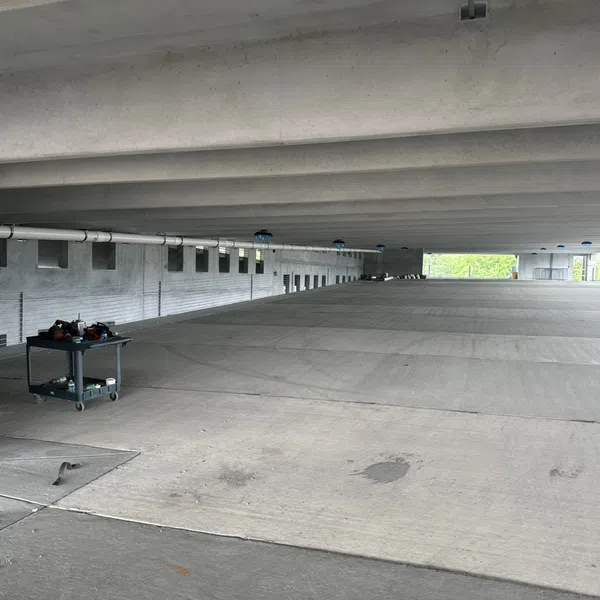 Empty concrete parking garage level with support beams and maintenance cart near white pipe under ceiling.