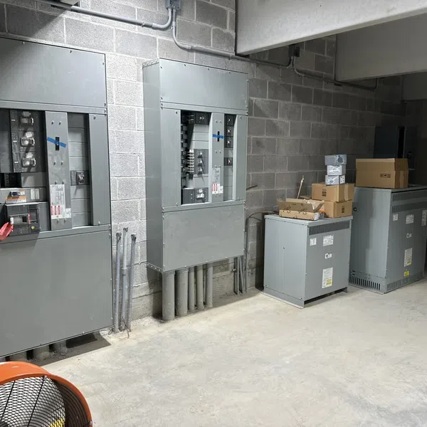Industrial electrical panels and transformer units installed in a concrete room with utility boxes and wiring.