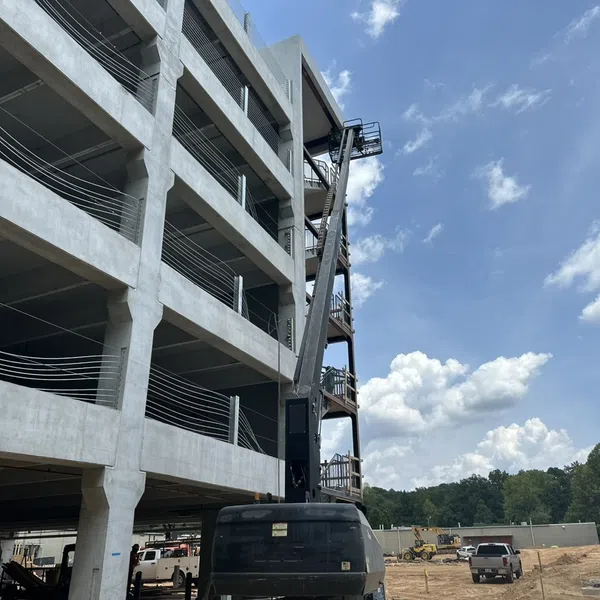 Construction site with a multi-story concrete building and a boom lift under a partly cloudy sky.