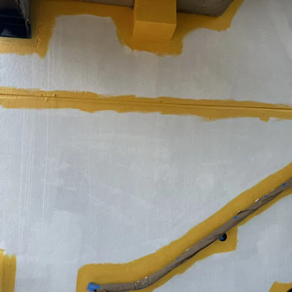 White wall with yellow trim and a handrail wrapped in masking paper along the stairs under construction.