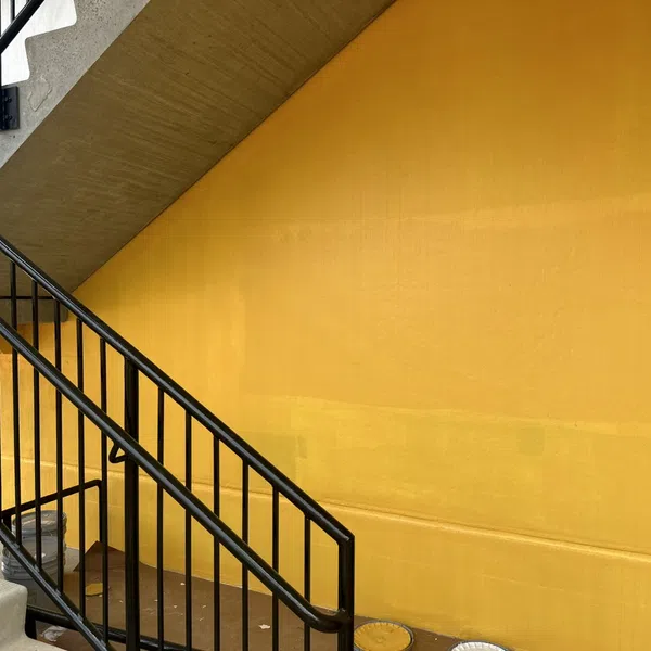 Concrete staircase with black metal railing against vibrant yellow wall background in modern urban setting