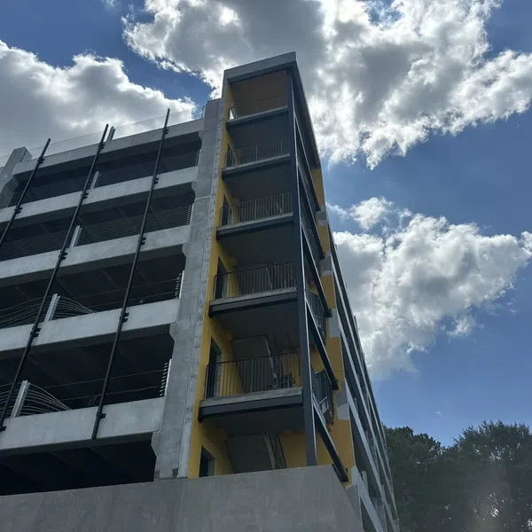 Modern multi-story parking garage with yellow stairwell against blue sky and white clouds outdoors.