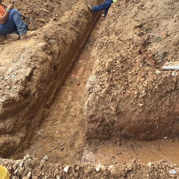 Two construction workers in a deep trench surrounded by brown dirt during excavation work.