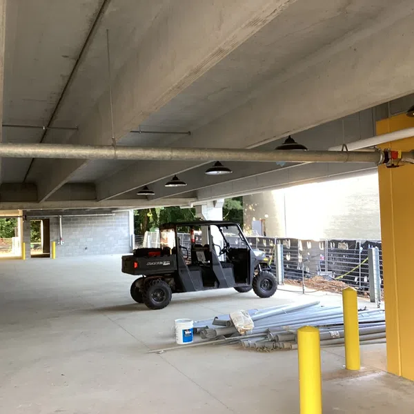 Utility vehicle parked inside a concrete parking garage with pipes and yellow posts near a yellow wall.
