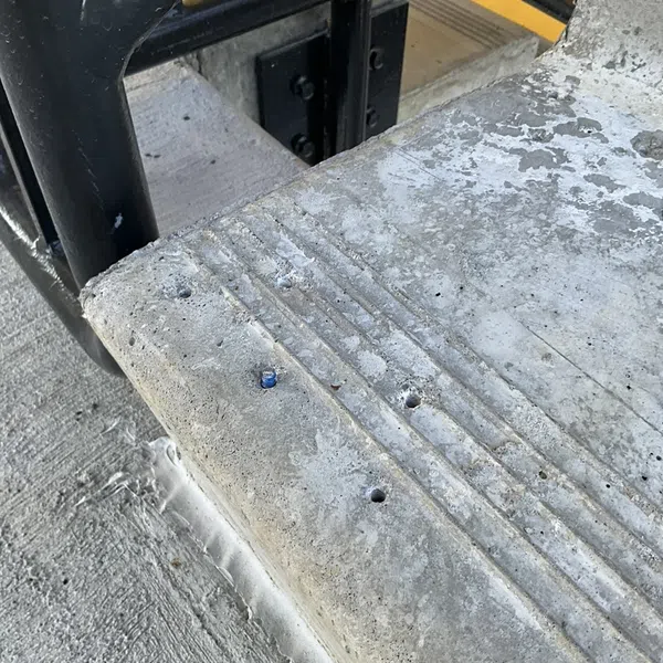 Close-up of worn concrete stair edge with metal railing and textured yellow safety strip in background.