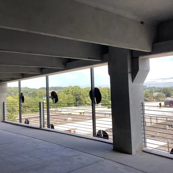 Concrete parking deck with metal railing and fans overlooking industrial buildings and trees.