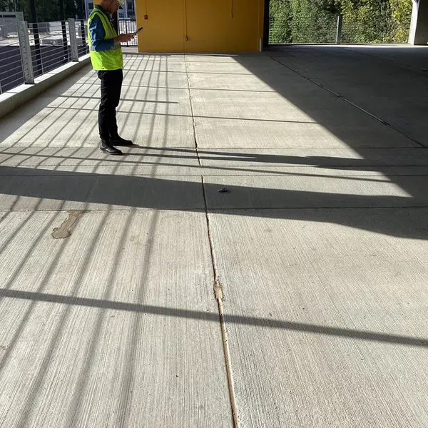 Man in safety vest standing in a sunlit parking garage casting long shadows on the concrete floor.