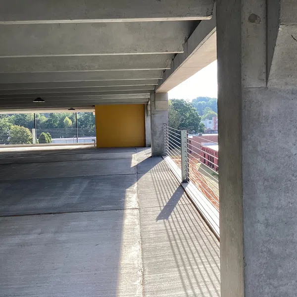 Empty concrete parking garage with yellow wall and metal railing casting shadows in sunlight.