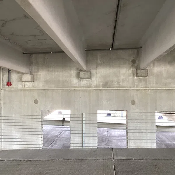 Interior of a concrete parking garage with horizontal metal railings and large rectangular openings letting in daylight.