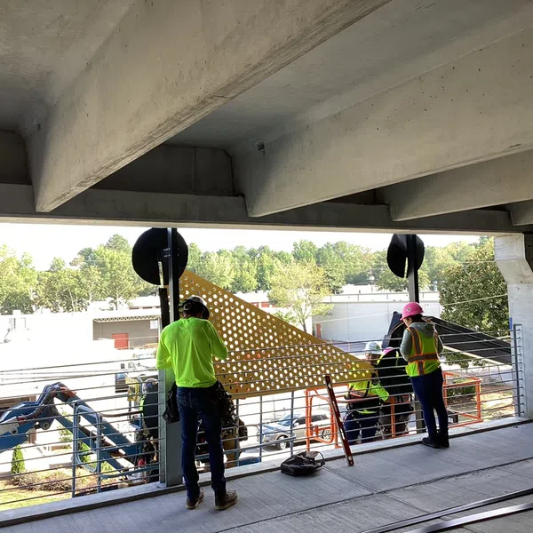 Construction workers in safety gear installing a large perforated panel on a building balcony during daylight.