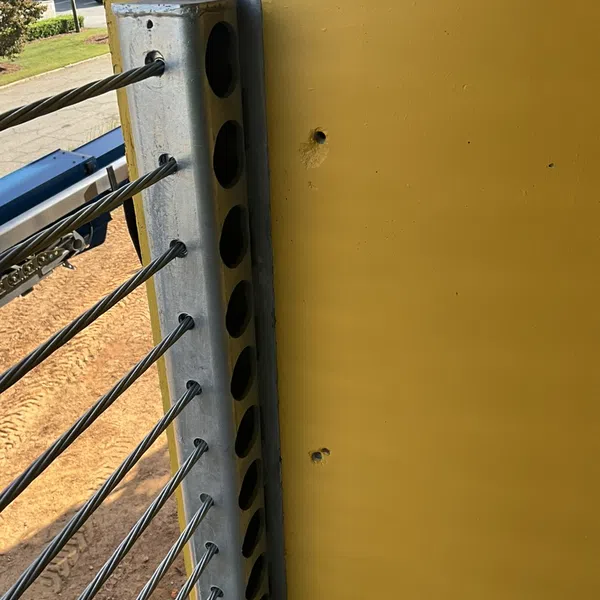Steel cable wires secured to a yellow structural steel beam with a metal anchor plate in an industrial setting.