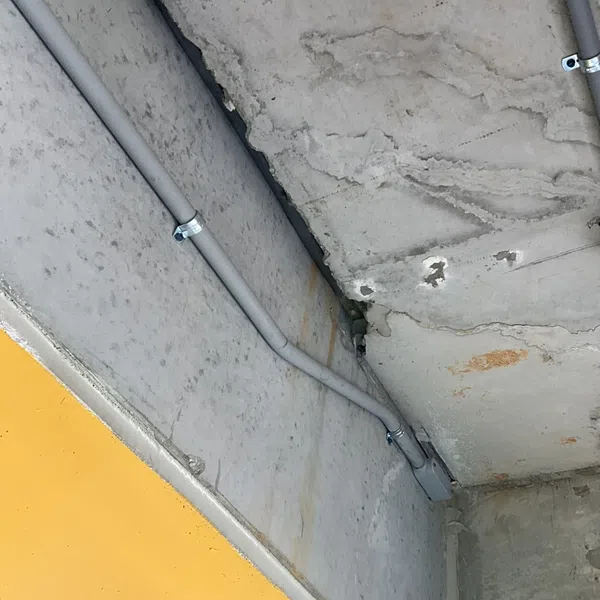 Gray electrical conduit pipes mounted on a concrete ceiling and wall with a yellow painted lower wall section.