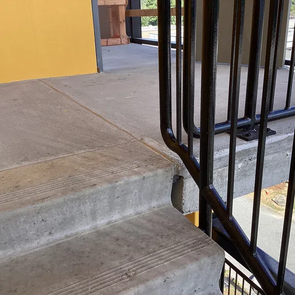 Concrete outdoor stairs next to a yellow wall with black metal railing on a sunny day.