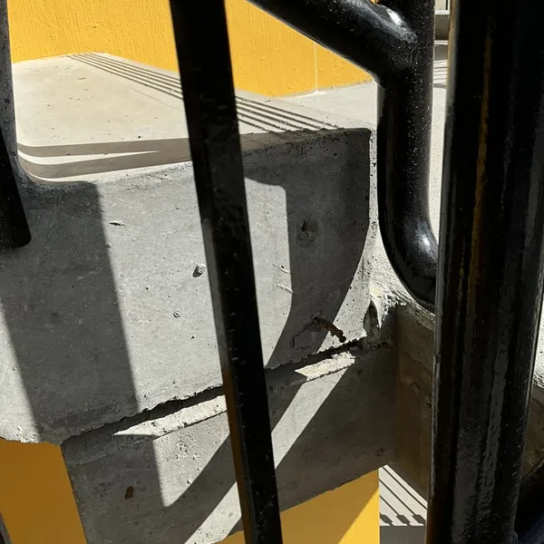 Close-up of concrete stair steps and black metal railing with bright yellow wall background in sunlight.