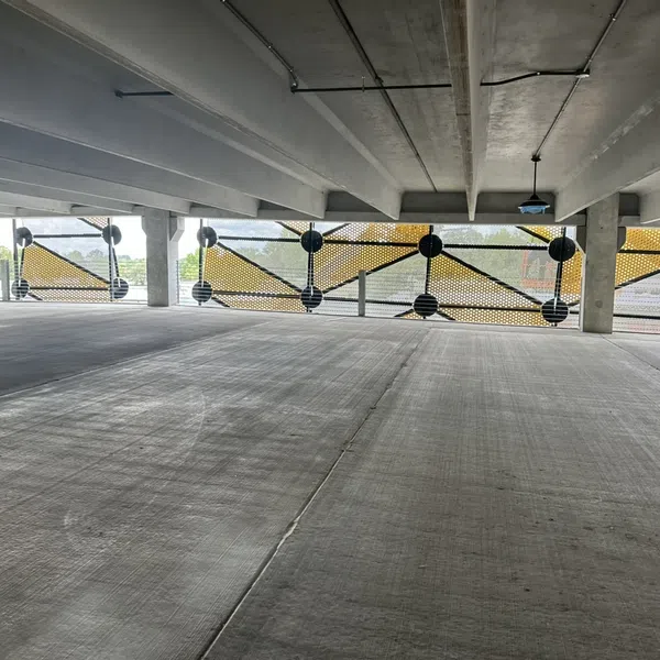 Empty concrete parking garage level with yellow mesh safety barriers and concrete beams overhead.