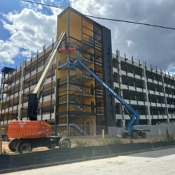 Construction site with workers using lift machines on a multi-story building under a cloudy sky.