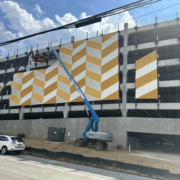 Construction workers install yellow and white chevron panels on multi-story parking garage exterior in daytime.