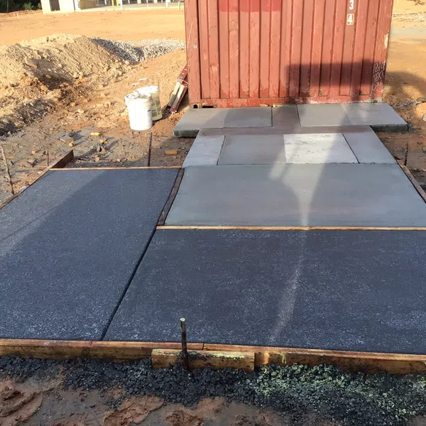 Freshly poured concrete slabs with wooden framing at a construction site near a red container.
