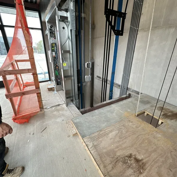 Construction worker inspecting elevator shaft installation with safety barriers and unfinished concrete floor.
