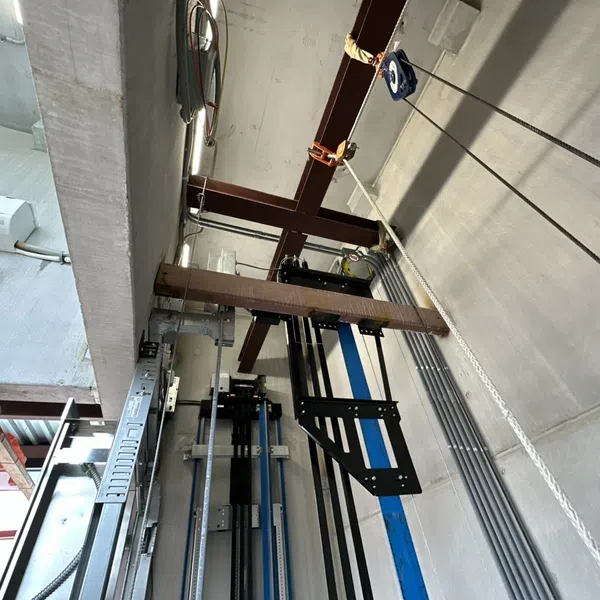 Industrial interior with steel beams, pulley system, concrete walls, and exposed electrical conduits in a warehouse.