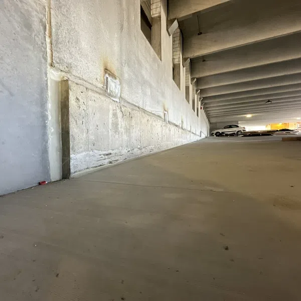 Empty concrete floor and wall in a multi-level parking garage with parked cars and overhead concrete beams.