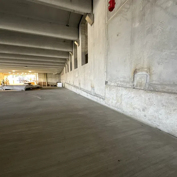 Empty concrete parking garage with ceiling beams and distant light at far end under construction or renovation.