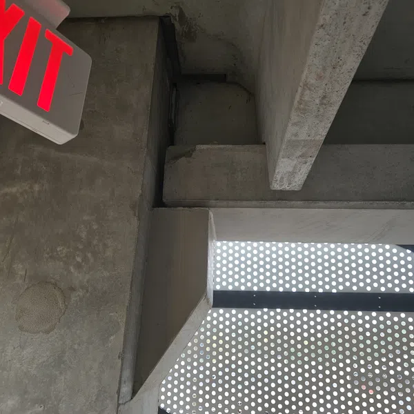 Concrete corner in a parking garage with a red EXIT sign and perforated metal panel wall.